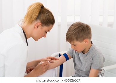 Young Female Doctor Taking Blood Sample Of Child Patient In Clinic