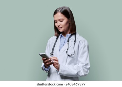 Young female doctor using smartphone, on green studio background - Powered by Shutterstock