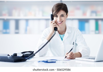 Young female doctor working at office desk and answering phone calls