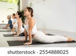 Young female doing cobra pose for health care and wellness with group together at modern yoga studio