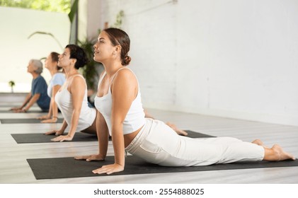 Young female doing cobra pose for health care and wellness with group together at modern yoga studio