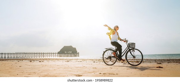 Young female dressed light summer clothes joyfully threw up her hand riding old vintage bicycle with front basket on the low tide ocean white sand coast on Kiwengwa beach on Zanzibar island, Tanzania. - Powered by Shutterstock