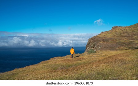 Young female dressed in orange waterproof jacket walking by the mountain above the cloud route on Madeira island, Ponta do Pargo, Portugal. Active people around World traveling concept.
