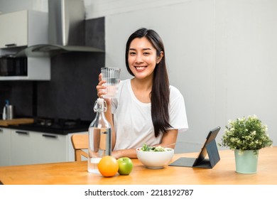 Young female drinking water in glass for refreshing for diet and wellness on table. Beautiful woman happily drink fresh water before breakfast in kitchen in the morning. Healthy food concept. - Shutterstock ID 2218192787
