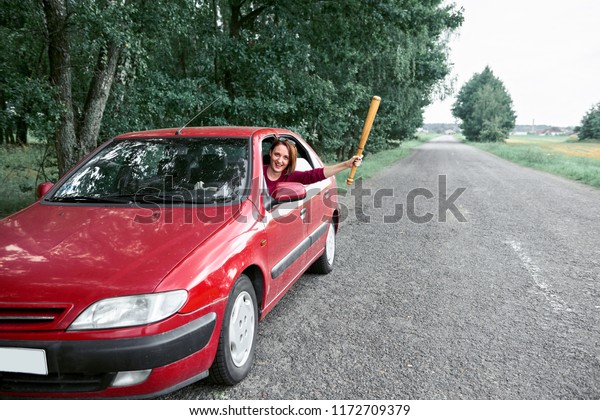 young female driver has stress and anger,\
threatens with a baseball bat, has a red\
car