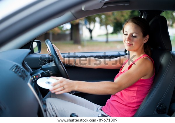 Young female driver playing music in\
the car - changing CDs (color toned image; shallow\
DOF)