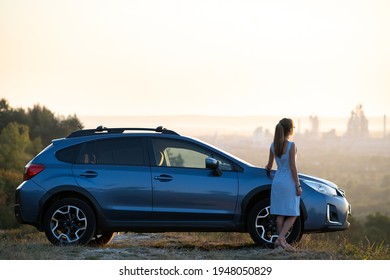 Young female driver resting near her car enjoying warm summer evening. Travel and getaway concept.
