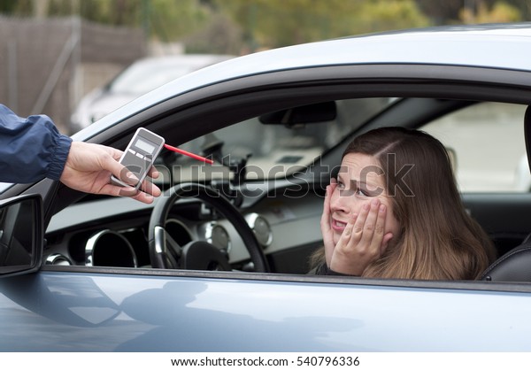 Young female driver subjected to\
breathalyzer test for alcohol content, surprised and in\
fear