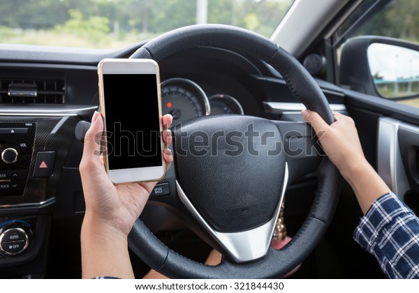 Young female driver using touch\
screen smartphone and hand holding steering wheel in a\
car.