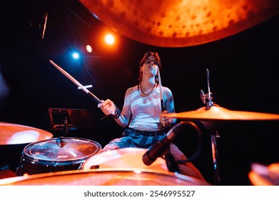 Young female drummer energetically playing the drums on a stage illuminated by colorful lights, creating a vibrant and dynamic musical performance - Powered by Shutterstock