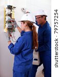 a young female electrician using an ammeter for checking an electricity meter and an older man watching her