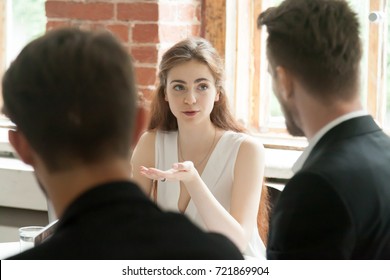 Young female employee sharing opinion with colleagues at work during briefing meeting. Corporate worker presenting new ideas to CEO or project managers. Coworking, teamwork and collaboration concept. 