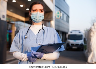 Young female EMS key worker doctor in front of healthcare ICU facility,wearing protective PPE face mask equipment,holding medical lab patient health check form,UK US COVID-19 pandemic outbreak crisis  - Powered by Shutterstock