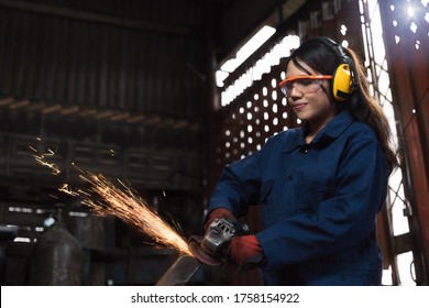 Young Female Engineer Operating Power Tools With Sparks In Manufacturing Workshop