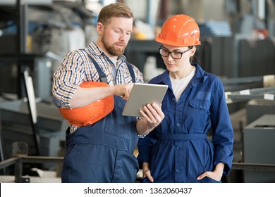 Young female engineer in uniform and helmet looking at tablet display while listening to colleague explanation of data - Powered by Shutterstock