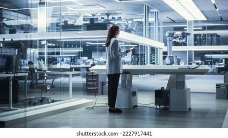 Young Female Engineer Using a Tablet Computer, Researching and Developing a Futuristic Robotic Arm Machine in a High Tech Industrial Laboratory with Modern Equipment. - Powered by Shutterstock