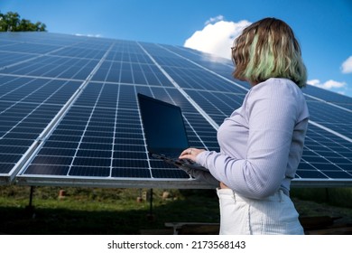 A Young Female Engineer Working With Solar Panels Programs And Optimizing Work Of The Solar Station. A Promising Young Female Engineer Is Setting Up Her Home Solar Power Plant  Green Energy Concept.