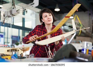 Young female enjoying her hobby - creating light airplanes in aircraft hangar
