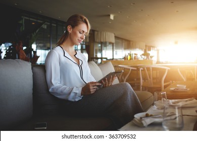 Young female entrepreneur reading electronic book on digital tablet during lunch in modern restaurant interior, elegant businesswoman chatting on touch pad while sitting in comfortable coffee shop - Powered by Shutterstock