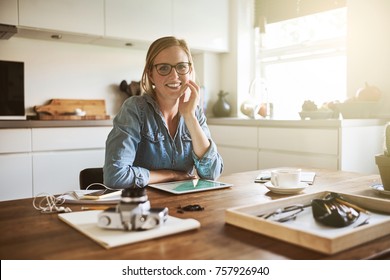 Young female entrepreneur smiling confidently while sitting alone at her kitchen table at home working on her small business - Powered by Shutterstock