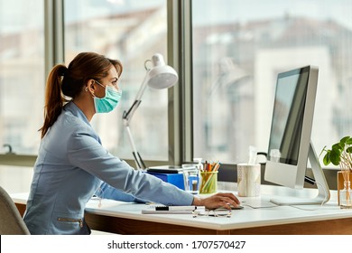 Young female entrepreneur wearing face mask while working on desktop PC in the office. 