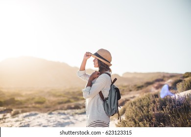 Young female exploring sandy beach with hat and backpack