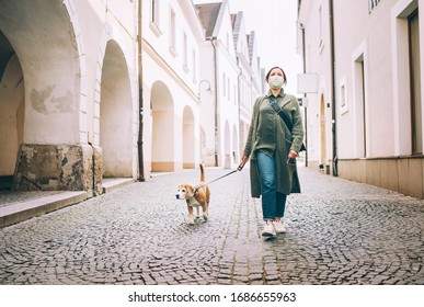 Young female fancy-dressed using a face mask as a coronavirus spreading prevention walking with her beagle dog on deserted old European squares and streets. Global COVID-19 pandemic concept image. - Shutterstock ID 1686655963