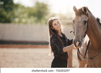 Young female farm owner taking care about a horse on an animal ranch on a summer day.