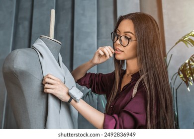 Young female fashion designer working with textile for sewing clothes. Dressmaker making create a new collection in her modern studio. Woman pinning cut out pieces of fabric to mannequin. - Powered by Shutterstock