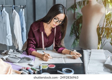 Young female fashion designer working in her atelier showroom workplace. Woman drawing a sketch in the studio. Clothing production, dressmaking, fashionable business seamstress concept - Powered by Shutterstock