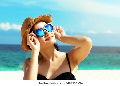 Young female fashion model smiling and wearing big sunglasses on a beach, sun protection and skincare concept.