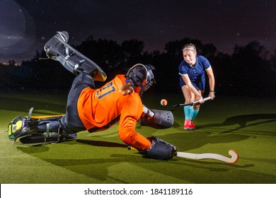 Young female field hockey player attacking the goalkeeper. Goalie defense the net in jump - Powered by Shutterstock