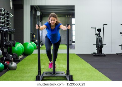 Young female fitness trainer performing sled push in local gym.