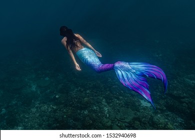 Young female free diver swims underwater in a colorful and sexy mermaid costume.