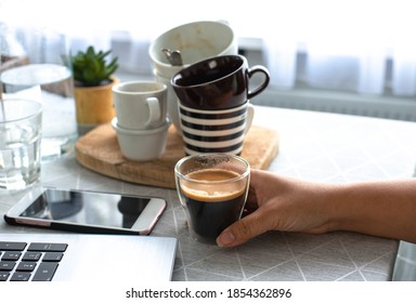 A young female freelancer  working from home holding a cup of coffee with many cups in the background drinks too much coffee caffeine addiction anxious and crazy in maniac bad lifestyle concept - Shutterstock ID 1854362896