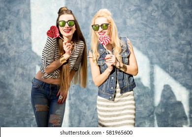 Young female friends having fun with candies standing on the blue wall background