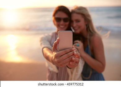 Young Female Friends On Vacation Taking Selfie On The Beach With A Smart Phone, Focus On The Hand And Mobile Phone.