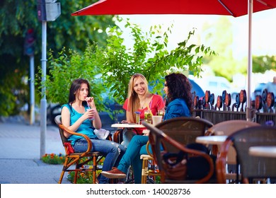 young female friends sitting on cafe terrace, urban outdoors