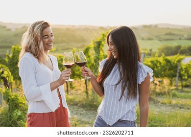 Young female friends tasting wine with wineyard in the background during sunset time - Happy women cheering with red wine outdoor - Powered by Shutterstock