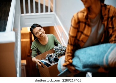 Young female friends walking up the stairs while carrying their belongings into a new home. Focus is on Asian woman.  - Powered by Shutterstock