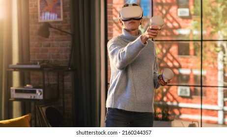 Young Female Gamer with Short Hair Having Fun and Playing Virtual Reality Game at Home in Her Living Room. She is Wearing a Modern Headset and Using Controllers. Stylish Apartment with Big Window. - Powered by Shutterstock