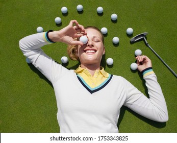 Young female golfer lying on green holding ball in front of eye view from above - Powered by Shutterstock