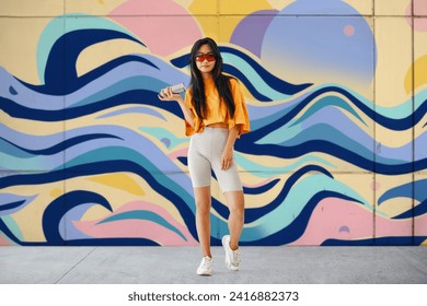 Young female graffiti painter standing near the wall with her paintings. Street art concept Full length portrait - Powered by Shutterstock