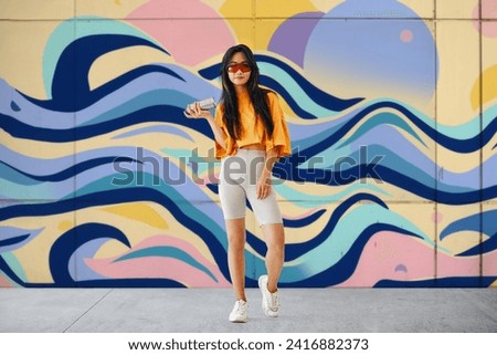 Young female graffiti painter standing near the wall with her paintings. Street art concept Full length portrait