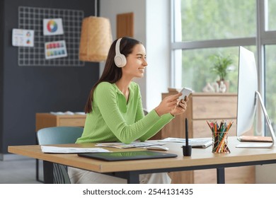 Young female graphic designer with headphones and tablet computer working at table in office - Powered by Shutterstock