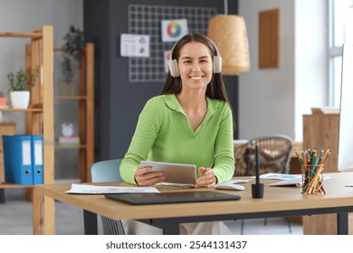 Young female graphic designer with headphones and tablet computer working at table in office - Powered by Shutterstock