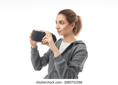 Young Female In Gray Hoodie Looking Away While Putting On VR Goggles Against White Background