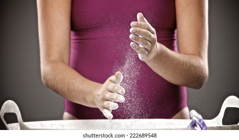 A Young Female Gymnast Is Chalking Her Hands To Prepare For Her Uneven Bar Routine.