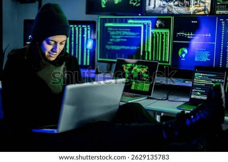 Young female hacker coding on laptop while breaching security system using multiple monitors displaying sensitive data and global network connections