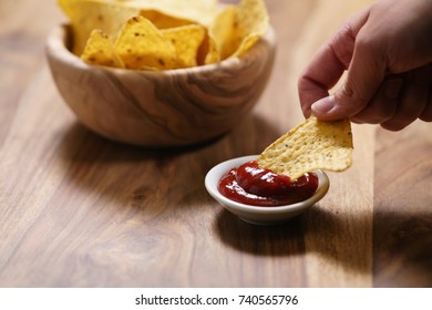 Young Female Hand Dipping Nachos In Tomato Salsa Sauce